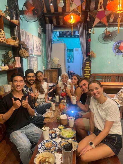 A group of people sitting around a table with food and drinks, in a room with wooden beams and decorative items. 1