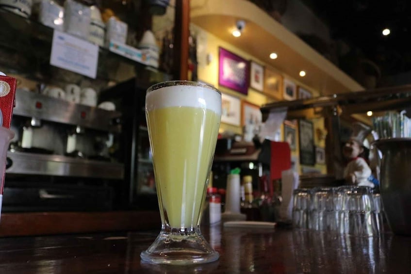 A tall glass of pale yellow beer with a white head on a bar counter. 1