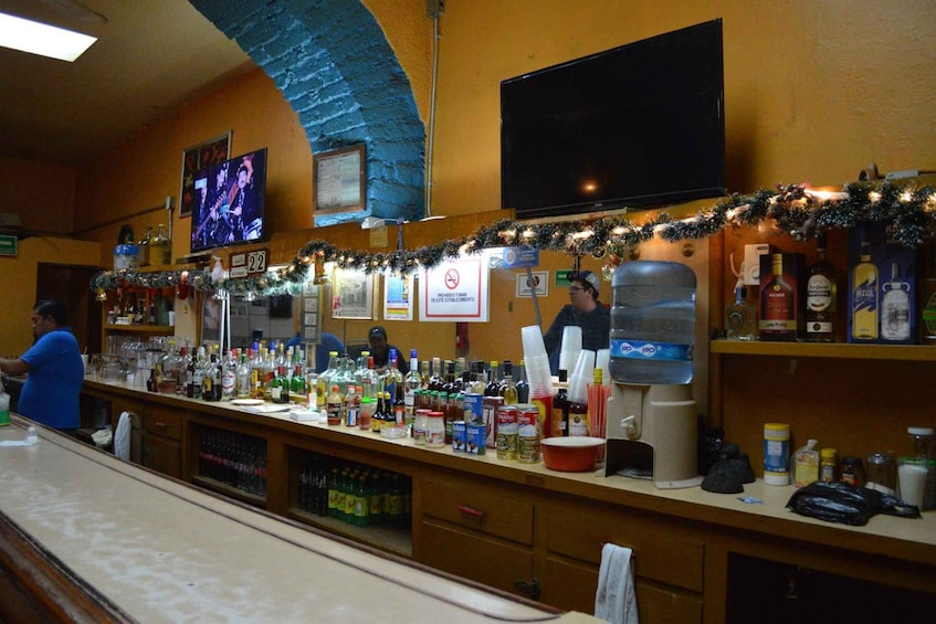 A bar with a counter, shelves with bottles, a TV, and festive decorations. 4
