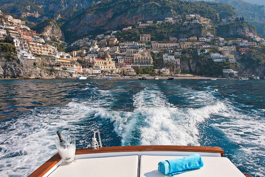 A boat moving through a coastal town with buildings on a hillside. 1