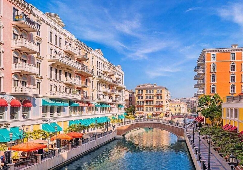 A canal with buildings on either side, a bridge, and outdoor seating areas with umbrellas. 2
