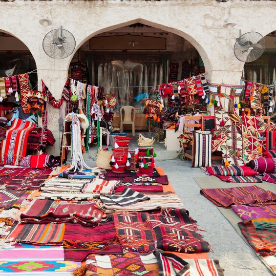 A market stall with colorful textiles and rugs displayed on the ground. 4