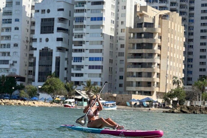 Une personne fait du kayak sur une planche de paddle rose, avec de grands immeubles en arrière-plan. 4