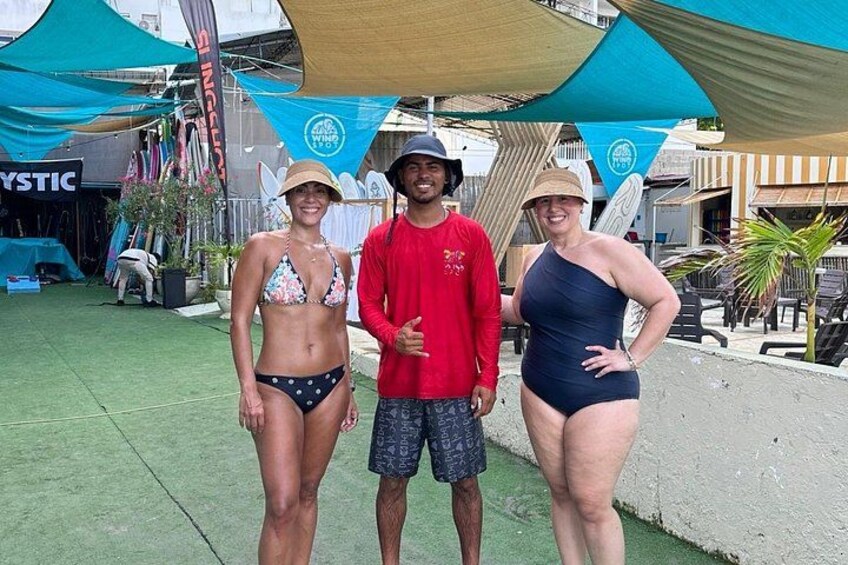 Trois personnes se tiennent sur une surface en béton, avec un parasol de plage et un panneau visible en arrière-plan. 5
