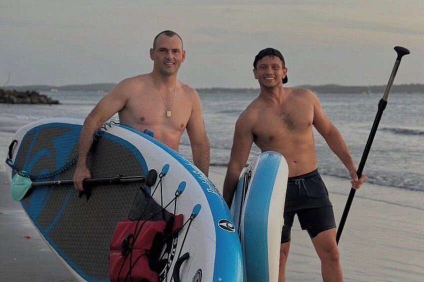 Deux hommes se tiennent sur une plage, chacun tenant une planche de paddle et une pagaie. 3
