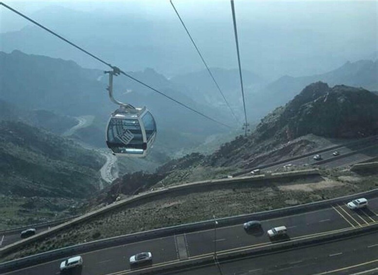 A cable car moving over a mountainous landscape with a highway below. 5