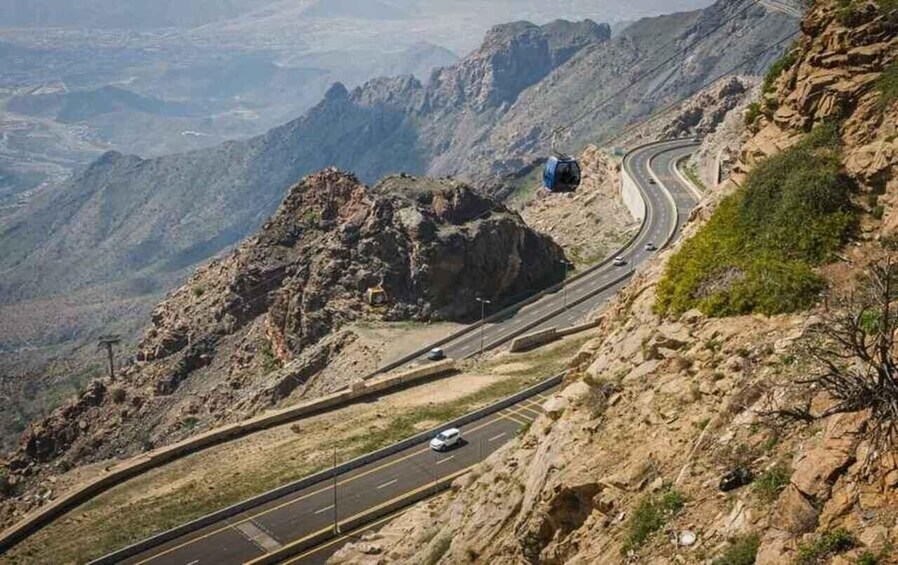 A winding mountain road with a blue cable car on the right. 4