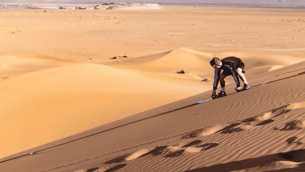 A person skiing down a sand dune in a desert landscape. 5
