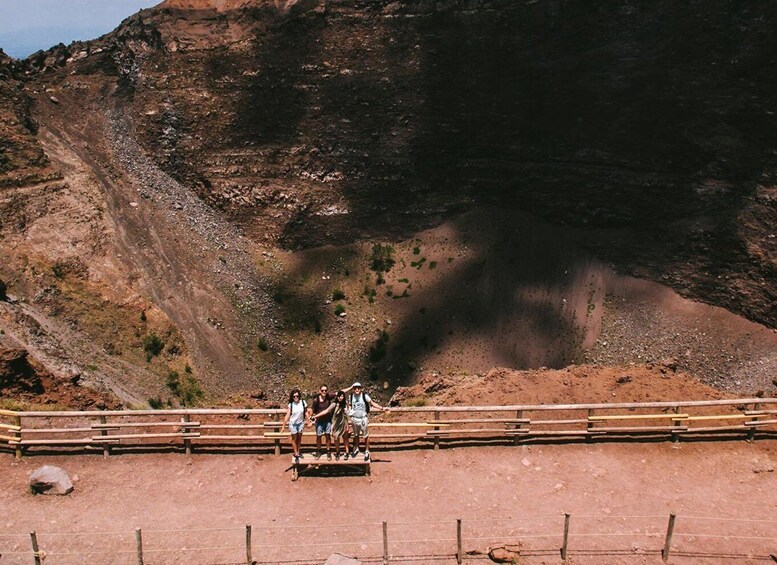 A group of people sitting on a wooden bench in a rocky landscape with a mountain in the background. 4