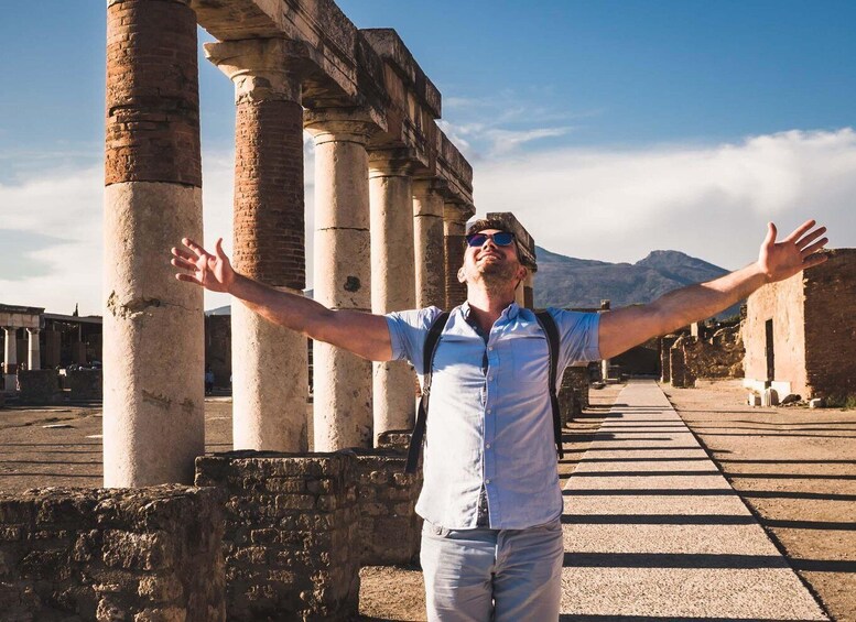 A person standing with arms outstretched in front of ancient stone columns. 5