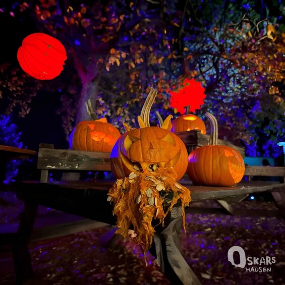 Carved pumpkins on a wooden table with autumn leaves and a red lantern in a garden at night. 5