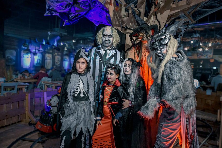 A group of people in Halloween costumes in a dimly lit indoor setting with tables and chairs. 3