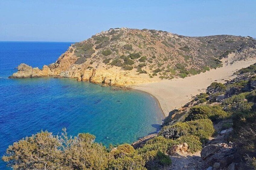 A coastal landscape with a sandy beach, clear blue waters, and a rocky hill with sparse vegetation. 3