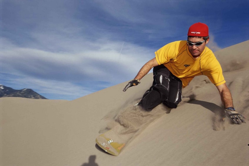 A person in a yellow shirt and red cap sliding down a sand dune. 3