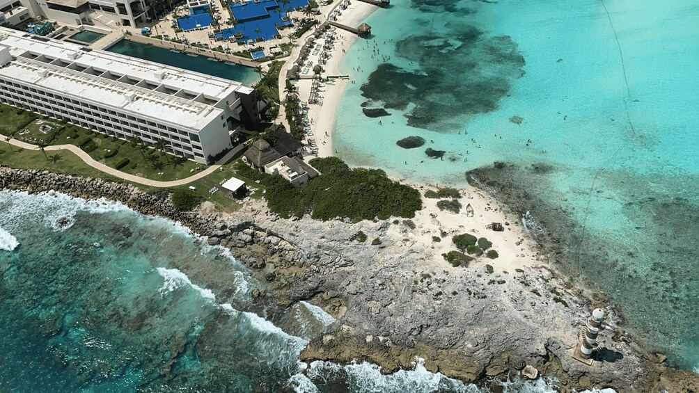 An aerial view of a coastal resort with a beach, clear turquoise waters, and a large hotel complex. 2