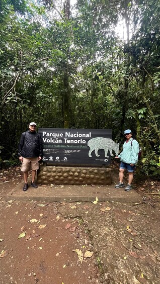 Two people standing in front of a sign for Parque Nacional Volcán Tenorio. 3