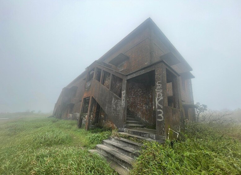 An abandoned, rusted building with graffiti, surrounded by overgrown grass and fog. 1