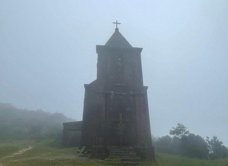 A solitary church tower with a cross on top, surrounded by foggy landscape. 2