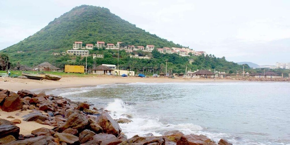 A beach with rocky foreground, calm water, and a hill with buildings in the background. 5