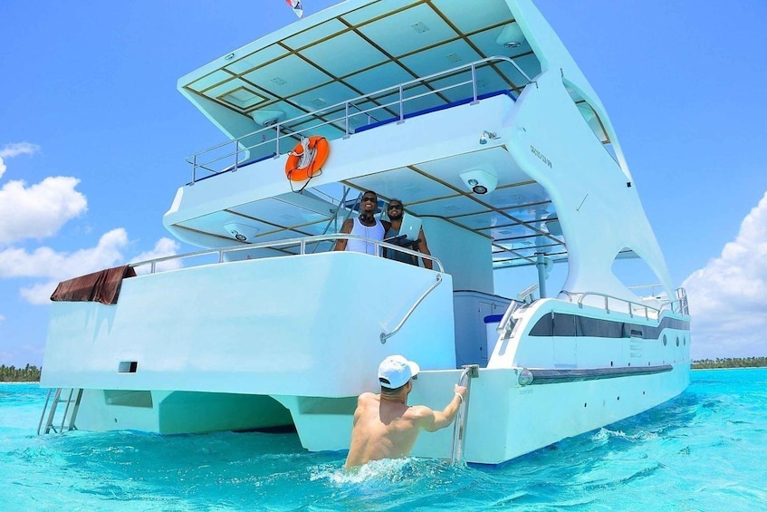 A white yacht with a person swimming in the water and another person on the deck. 2