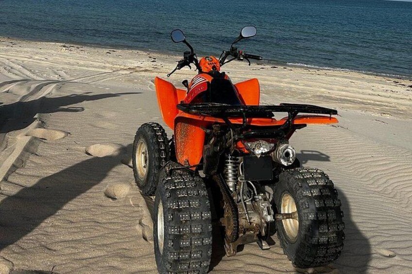An orange ATV parked on a sandy beach with the ocean in the background. 3