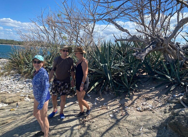 Three people walking along a rocky shoreline with sparse vegetation and a clear sky. 5