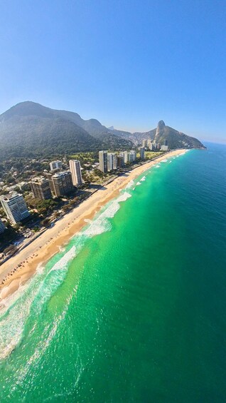 A coastal cityscape with a beach, ocean, and a mountain. 3