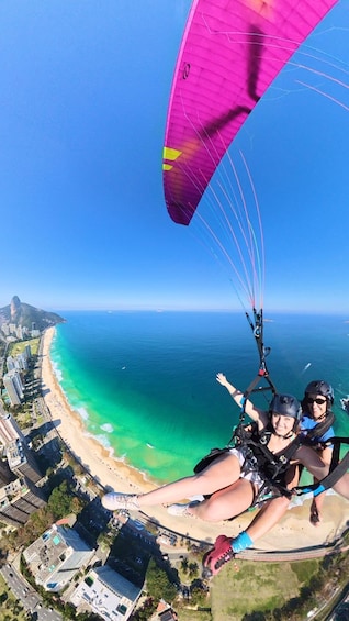 A person paragliding over a coastal area with buildings and a beach below. 1