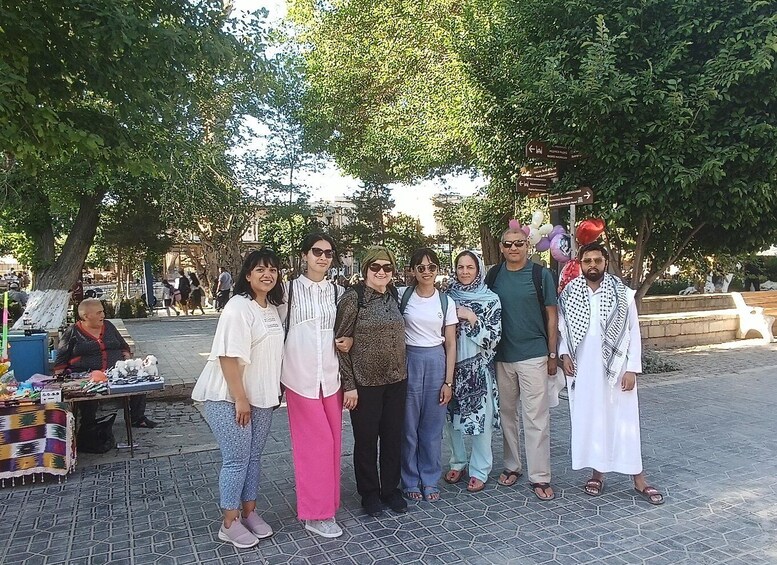 A group of people standing in a park with trees and a market stall in the background. 2