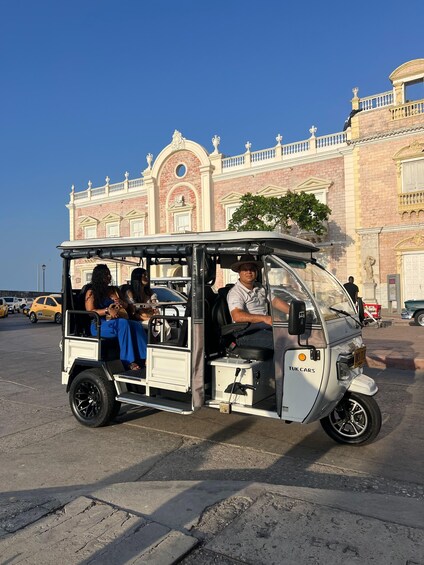 A tuk tuk with passengers, parked in front of a historic building with ornate architecture. 3