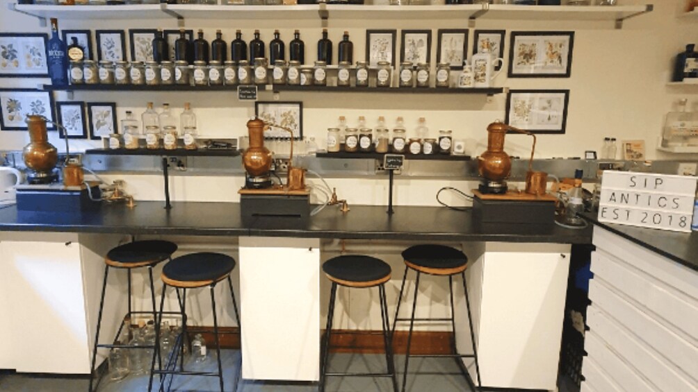 Un bar avec des tabourets, des étagères remplies de bouteilles et une enseigne indiquant : « SIP ANTICS, fondé en 2018 ». 2