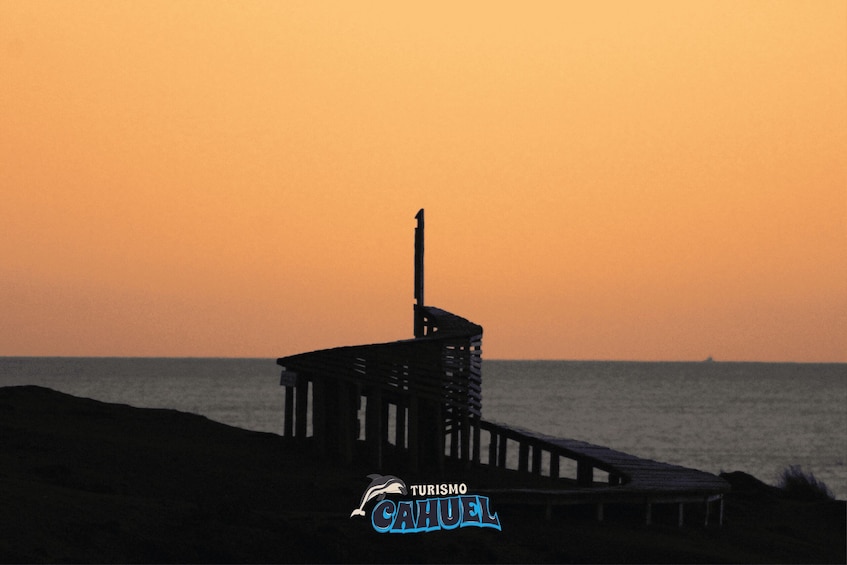 A pier at sunset with a logo for 'Turismo Cajuela' in the foreground. 4