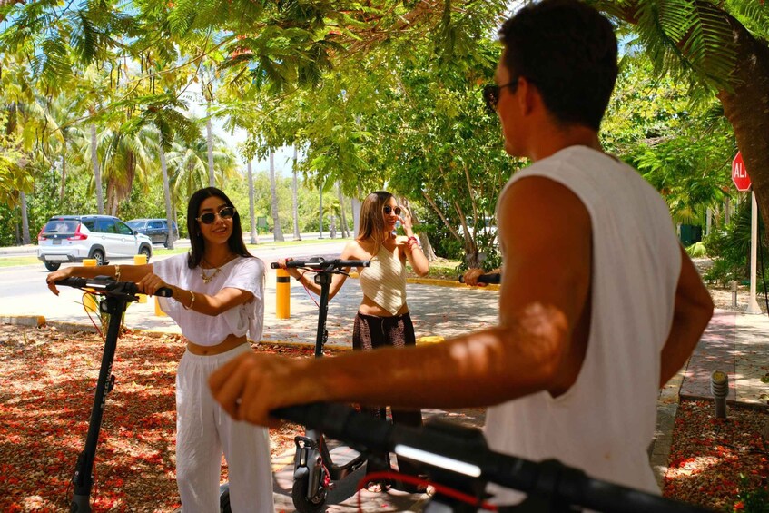 Three people on electric scooters on a tree-lined street. 5