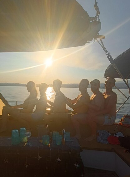 A group of people on a boat at sunset with drinks on the table. 2