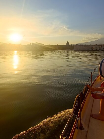 A boat on calm water with a sunset in the background and a distant cityscape. 3