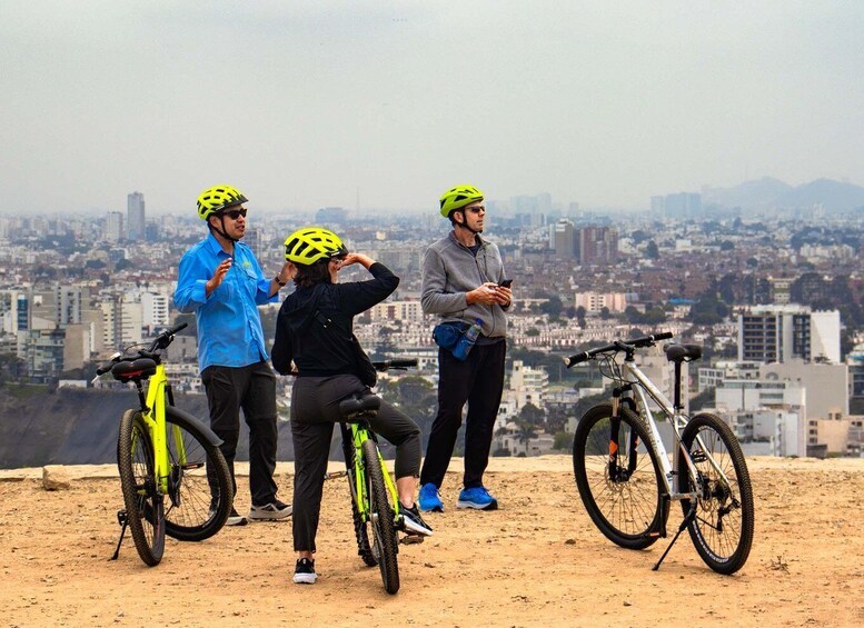 Three people on a hilltop overlooking a cityscape with bicycles. 1