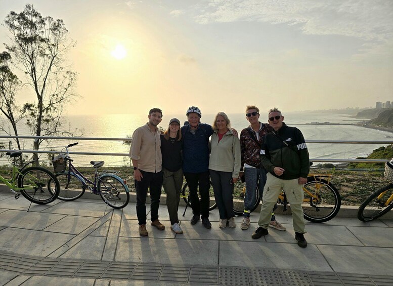 A group of people standing on a waterfront promenade with bicycles and a sunset in the background. 4
