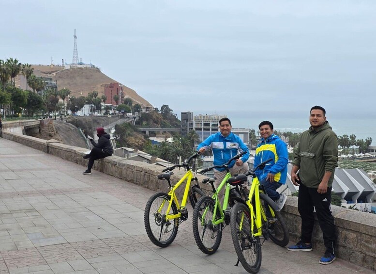 Three people standing by a waterfront promenade with bicycles. 5