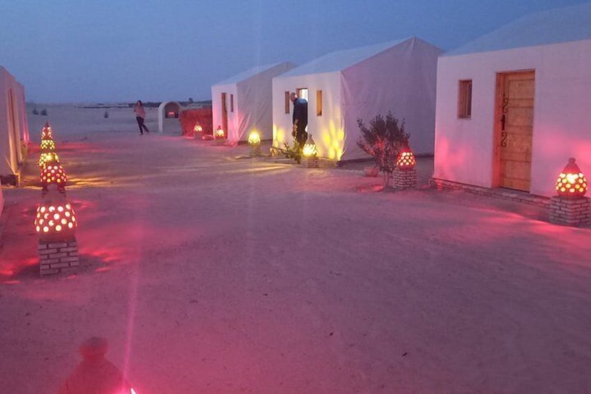 Ein Wüstencamp mit weißen Zelten, beleuchtet durch rote Lichter, und ein Weihnachtsbaum im Vordergrund. 2