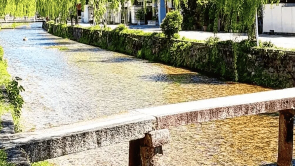 A stone bridge over a calm waterway, surrounded by greenery and buildings. 2