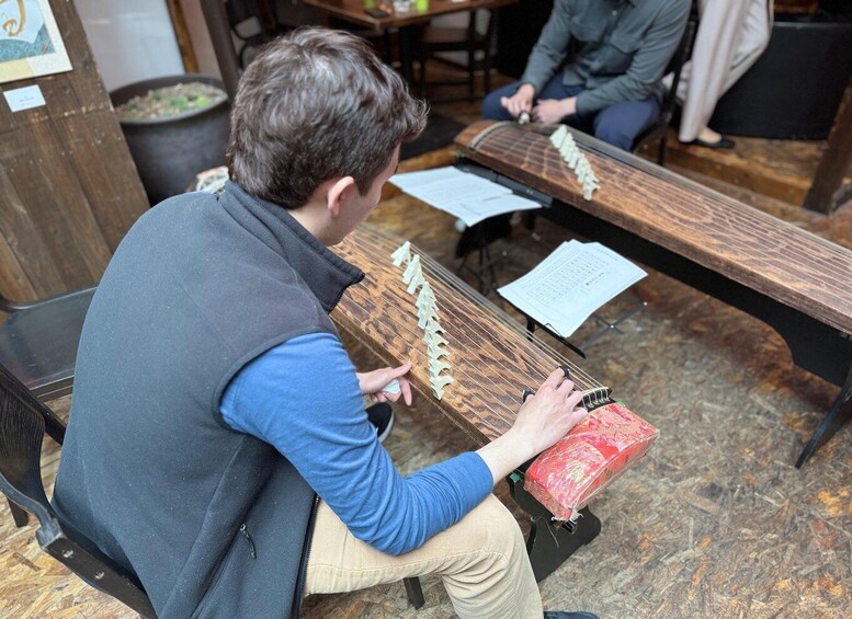 A person playing a stringed musical instrument, seated on a bench with sheet music. 5