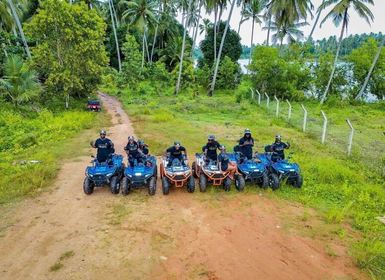 A group of people on all-terrain vehicles on a dirt path surrounded by lush greenery and palm trees. 3
