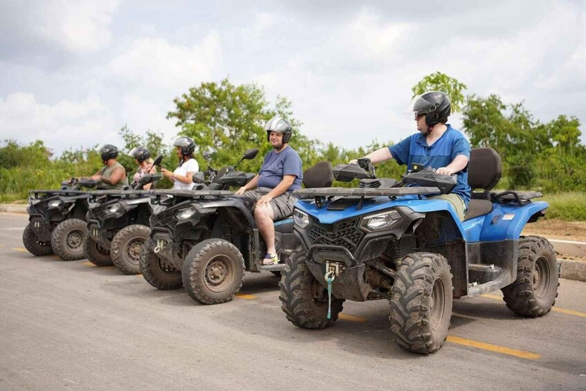 A group of people riding ATVs on a paved road with greenery in the background. 4