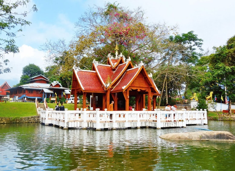 A traditional wooden pavilion on a floating platform in a body of water, surrounded by lush greenery and a clear sky. 2