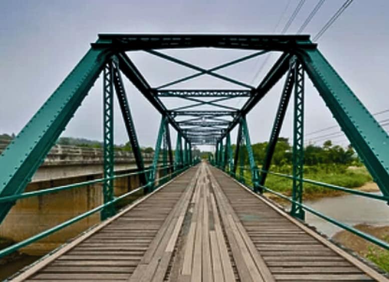 A green metal bridge with a wooden walkway over a river. 5