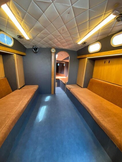 A train interior with blue flooring, wooden benches, and a ceiling with a geometric pattern. 5