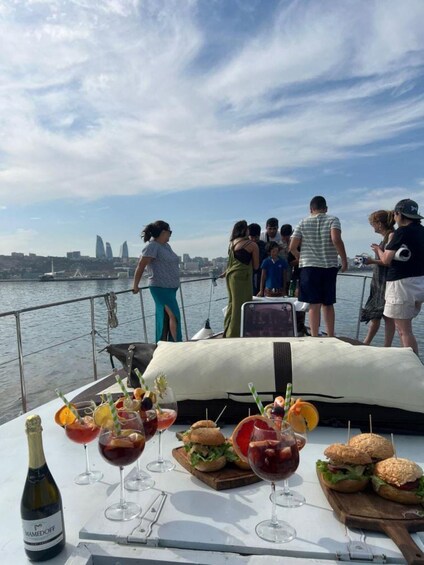 A boat with a table set for drinks and sandwiches, people standing on the deck, and a city skyline in the background. 2