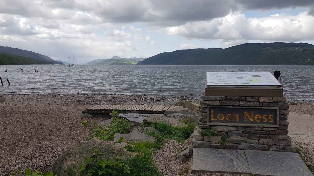 A rocky beach with a sign reading "Loch Ness" and a wooden pier extending into the water. 1