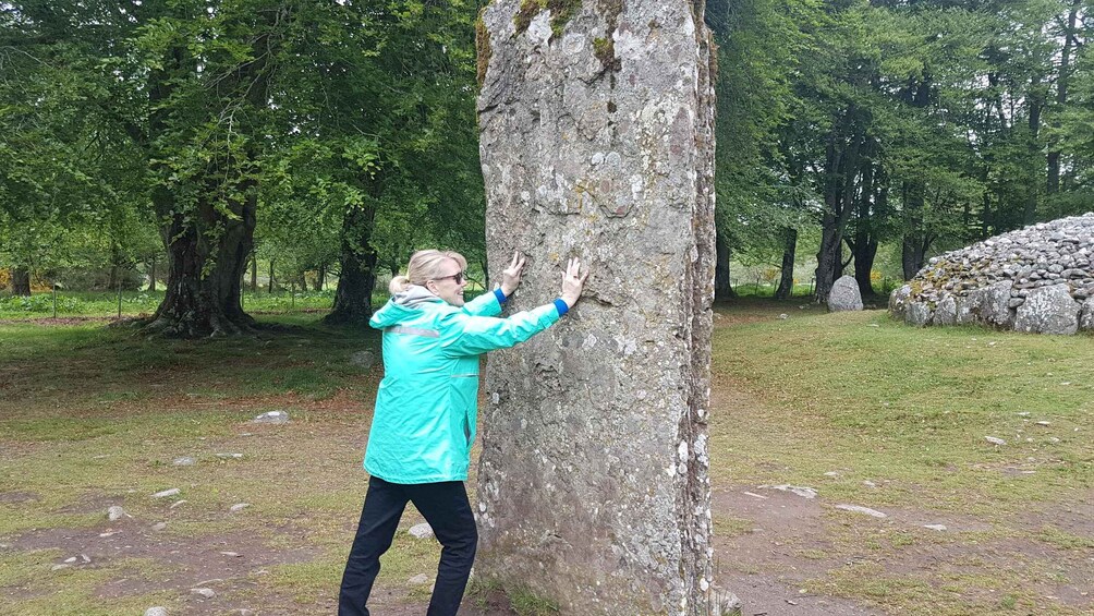 A person touching a tree trunk in a forested area with a stone structure in the background. 4