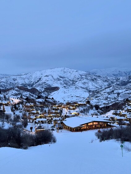 Une chaîne de montagnes enneigées, avec un village à ses pieds, où l’on peut admirer des bâtiments illuminés et un chalet imposant. 1